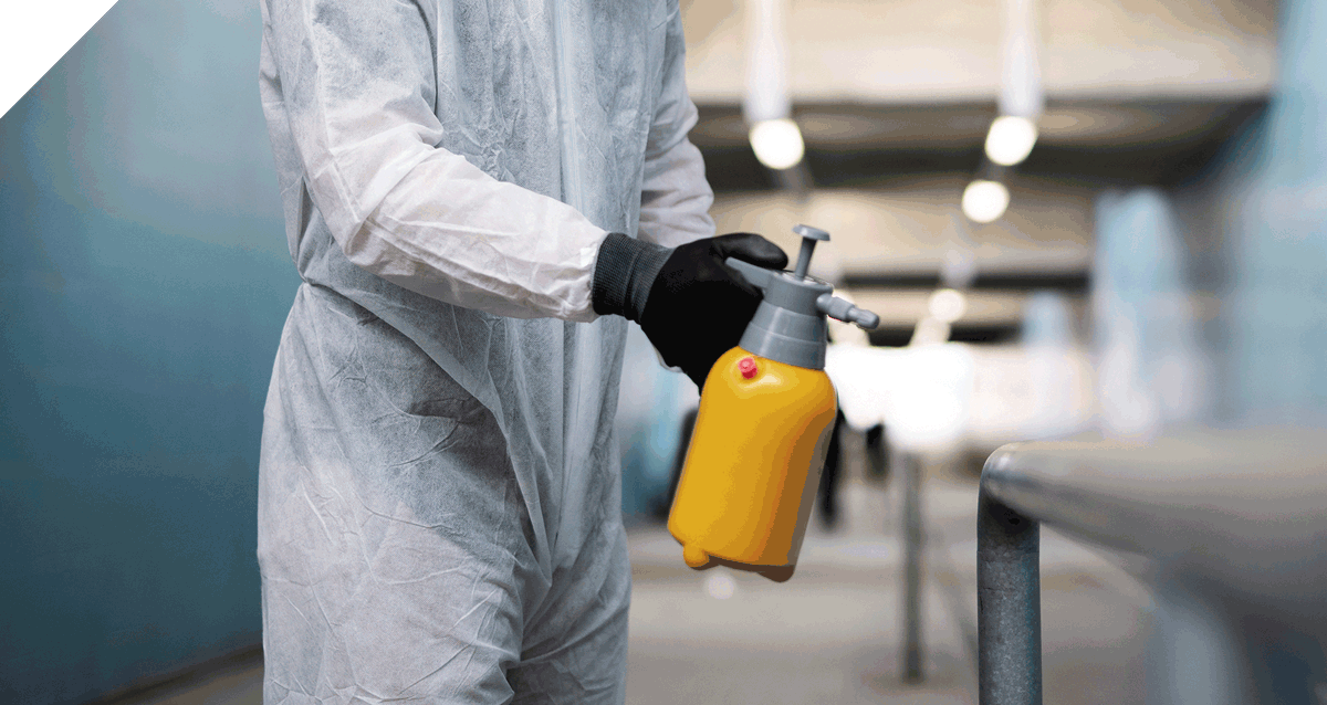 Fachkraft bei der Desinfektion im sensiblen Hygienebereich mit Schutzanzug und Sprühflasche